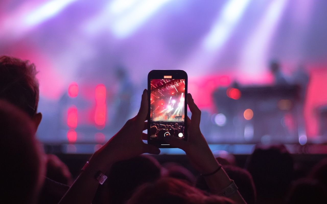 social-feed-img-04 A vibrant concert scene with an audience member recording the performance on a smartphone in Bentonville, AR.