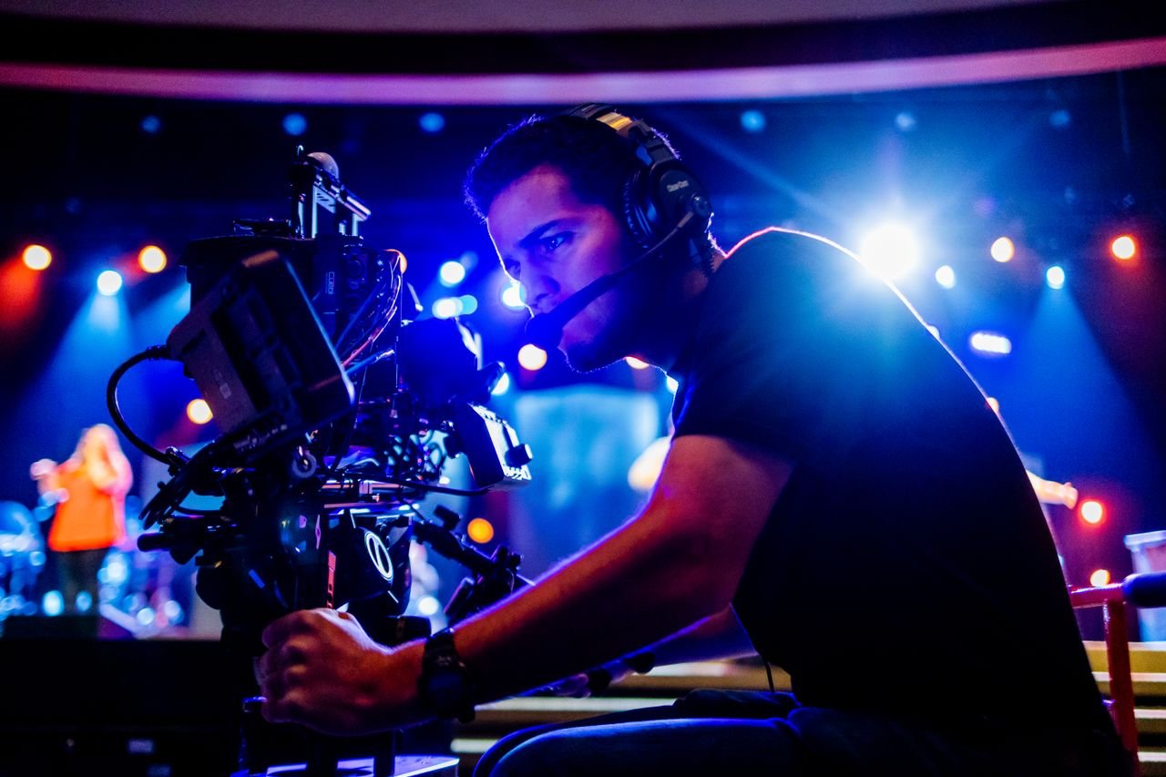 bachelor-party-03 Focused cameraman using advanced equipment at a vibrant stage event, under colorful stage lights.