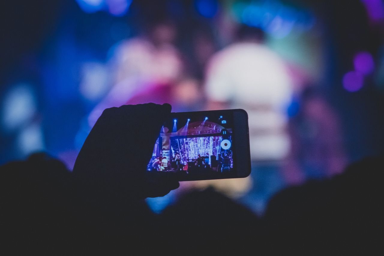 private-party-05 A hand holds a smartphone recording a live concert with vibrant lights.
